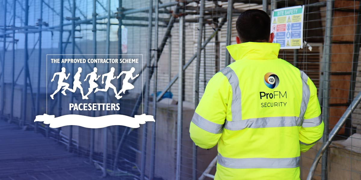 A ProFM security guard in a yellow high-visibility jacket, viewed from behind, standing by a construction site fence