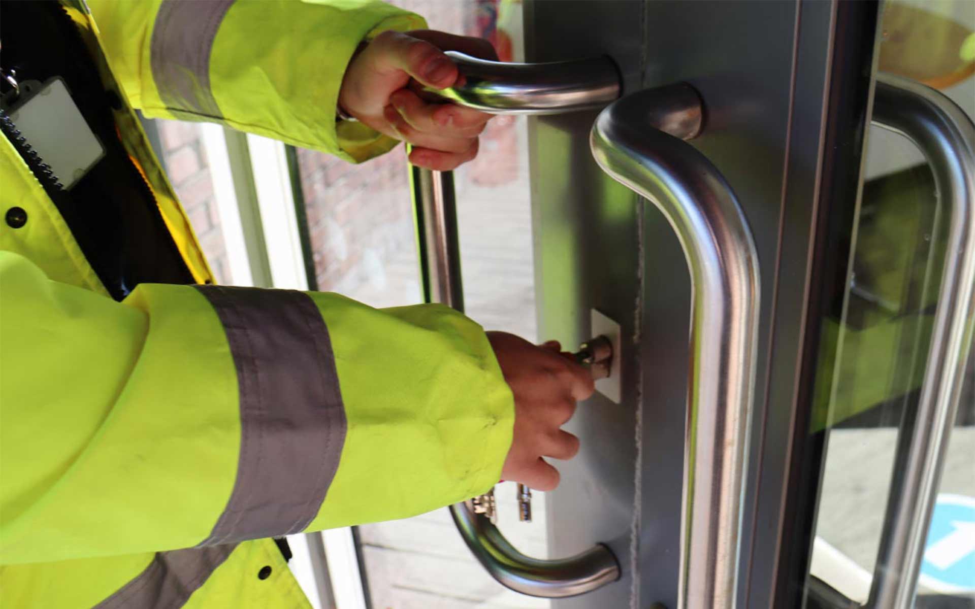 A close-up of a worker in a high-visibility jacket using a key to open a secure glass entrance door