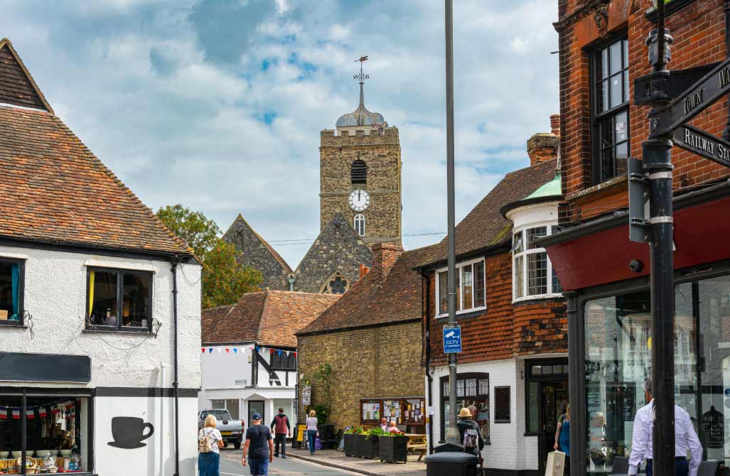 A traditional town center street in the South East featuring public CCTV monitoring signposts near local businesses