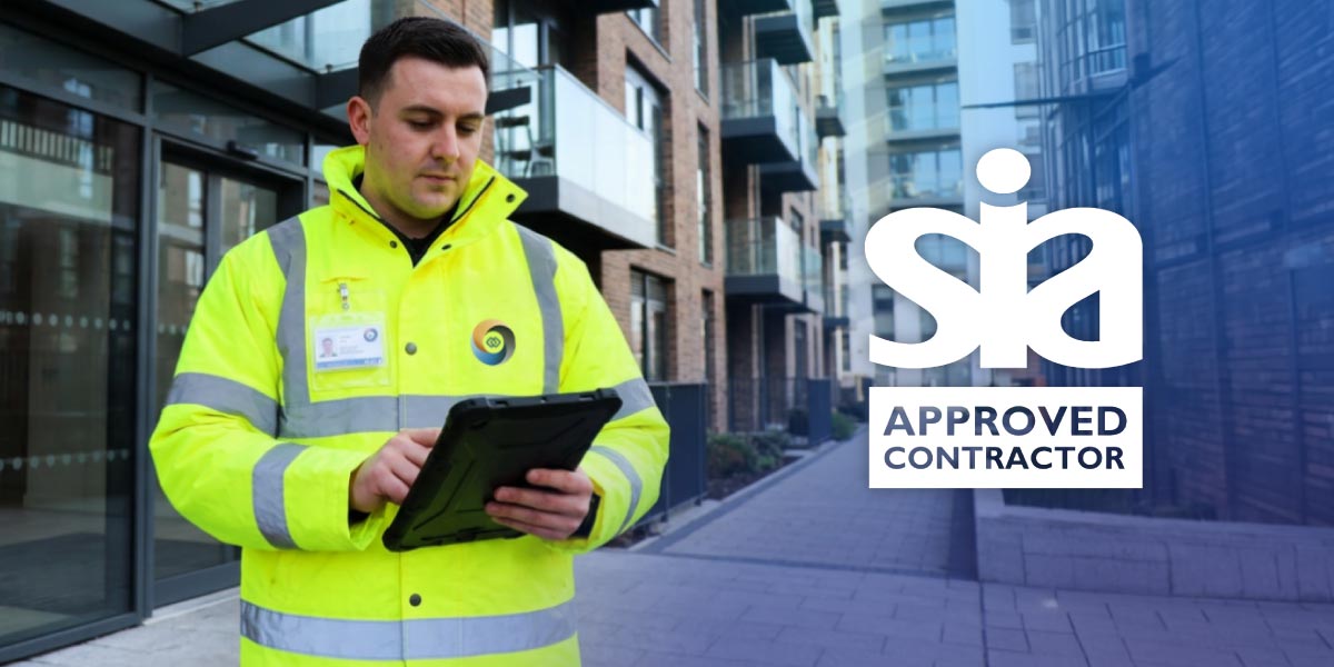 A security guard wearing a yellow high-visibility jacket using a tablet outside a modern apartment building
