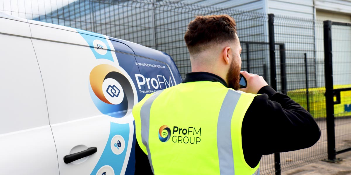 A ProFM security guard wearing a high-visibility vest talking on a radio next to a branded company patrol van