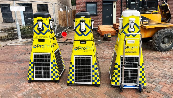 Three yellow ProFM VPOD wireless security towers standing on a brick paved driveway at a housing development.
