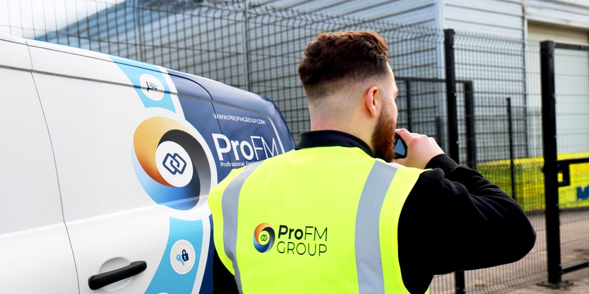 A ProFM mobile security response officer speaking into a radio next to a branded patrol vehicle outside a secure facility.