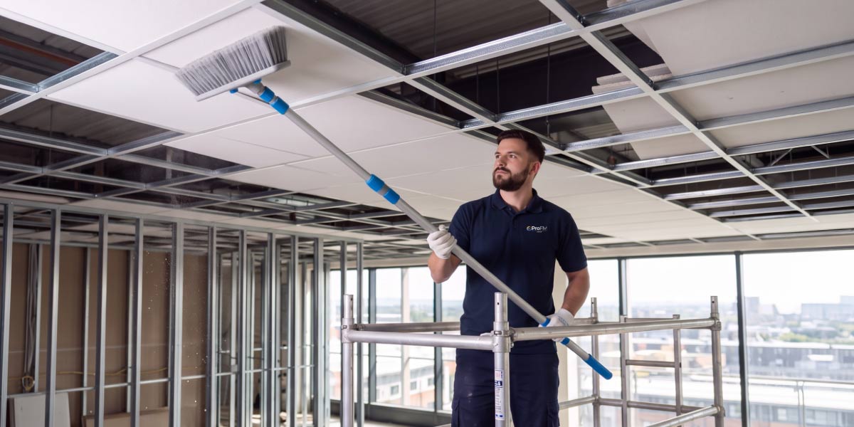 Builders cleaning operative removing construction dust from ceiling panels within a commercial fit out project during a post-construction clean.