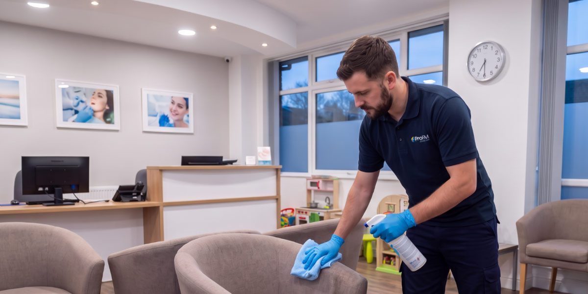 Professional cleaner disinfecting chairs and touchpoints in a dental practice waiting room as part of a dental cleaning programme.