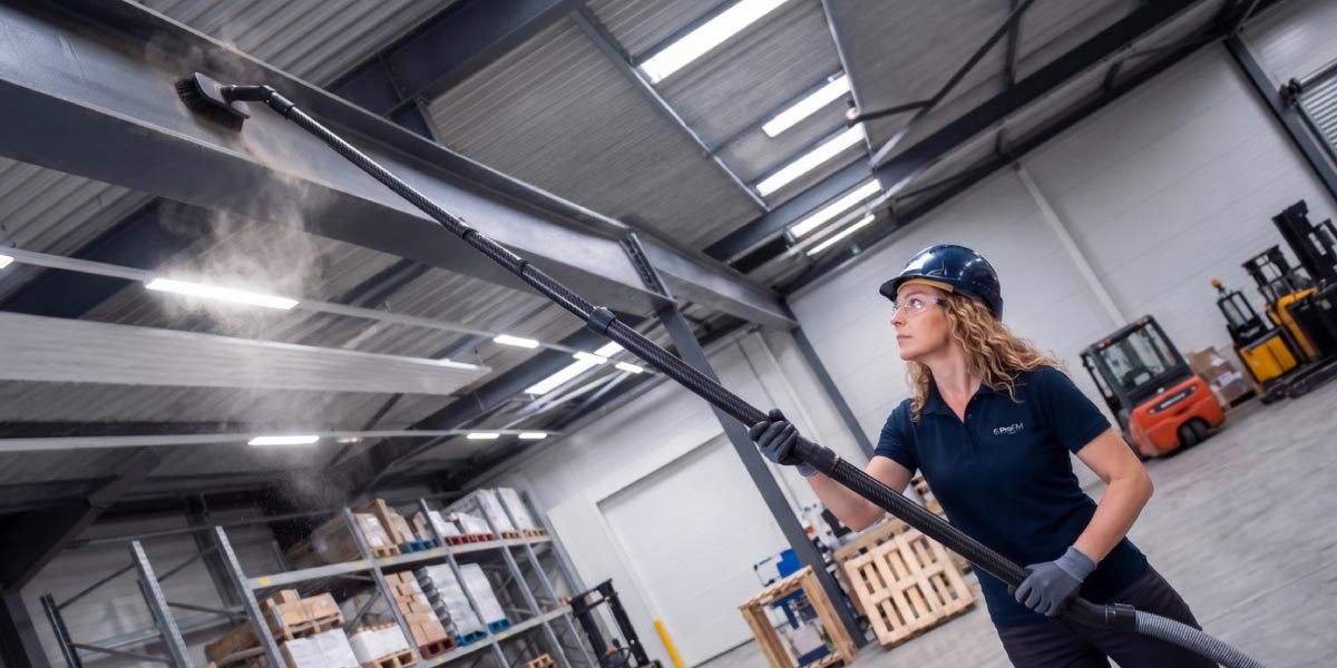 Industrial cleaning operative carrying out high-level factory cleaning to remove dust from structural steelwork within a manufacturing facility.