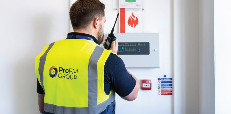 ProFM Group officer carrying out fire watch duties and monitoring a fire alarm control panel at a commercial laundry facility.