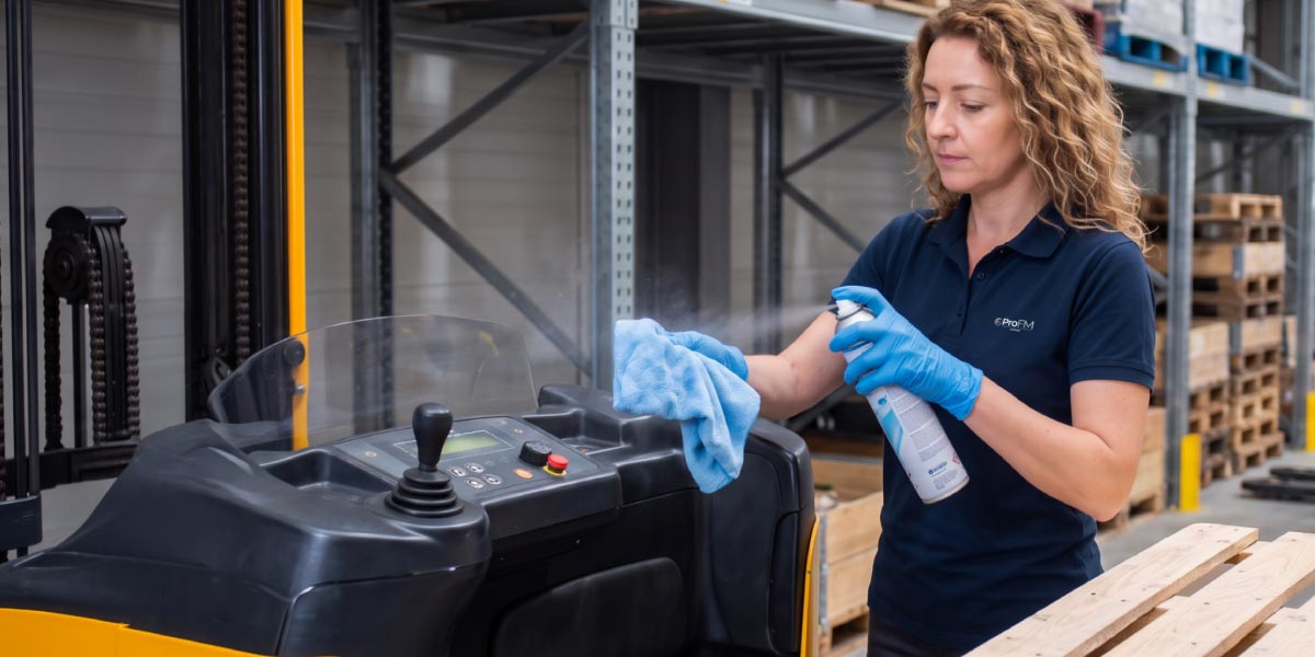 Warehouse cleaning operative sanitising forklift equipment within a warehouse to maintain cleanliness, safety and operational efficiency.