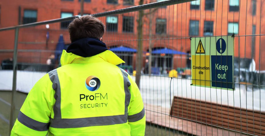 ProFM security officer standing beside construction site fencing and access control signage while monitoring a building site perimeter.