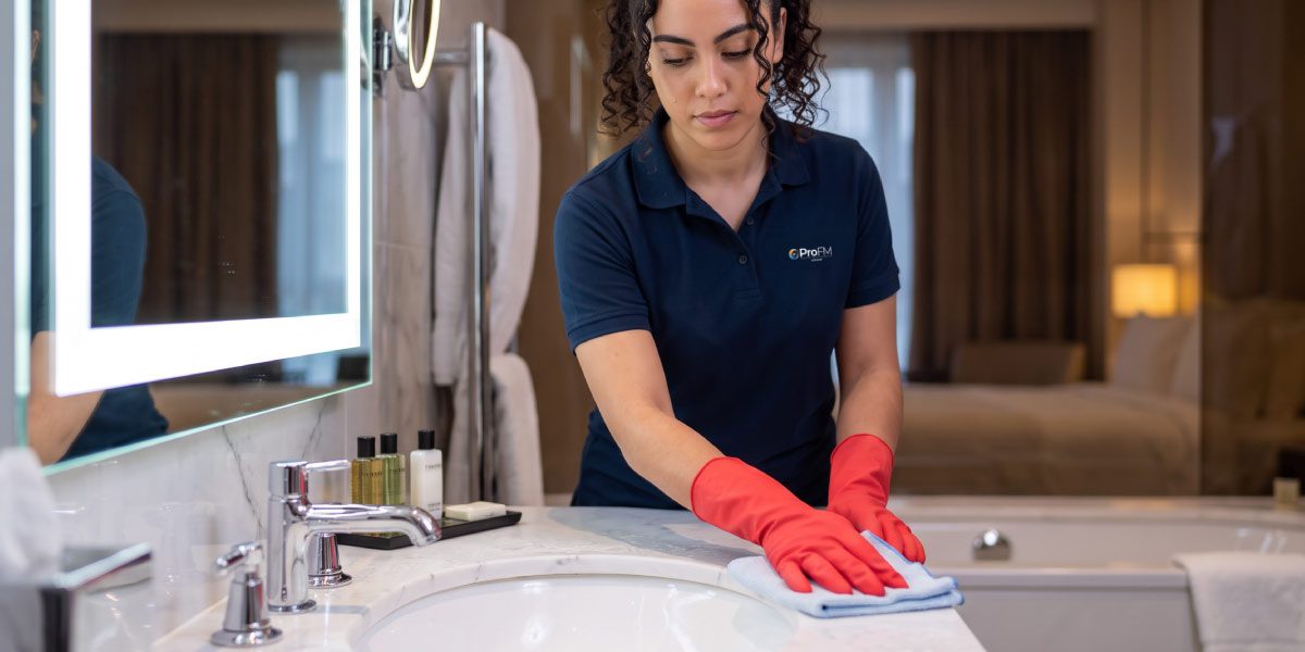 Professional cleaner disinfecting bathroom surfaces within a hotel guest room as part of a hotel cleaning service.